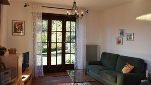 Una sala de estar con un sofá verde, un televisor de pantalla plana, una mesa de centro de vidrio y una araña.