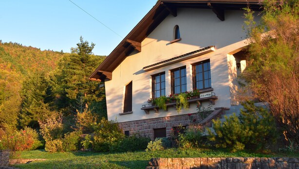 Una casa de dos pisos con base de piedra, ventanas grandes y un balcón con macetas.