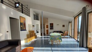 A spacious living area with a sofa, a coffee table, and a dining table with chairs. There are bookshelves and a staircase leading to an upper level. - In front... only the sea (Carqueiranne)