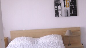 A bedroom with a wooden headboard, a white textured bedspread, a bedside lamp, and a wall art piece above the bed. - In front... only the sea (Carqueiranne)