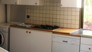 A compact kitchen with white cabinets, a gas stove, a dishwasher, and a window with a view of greenery. - In front... only the sea (Carqueiranne)