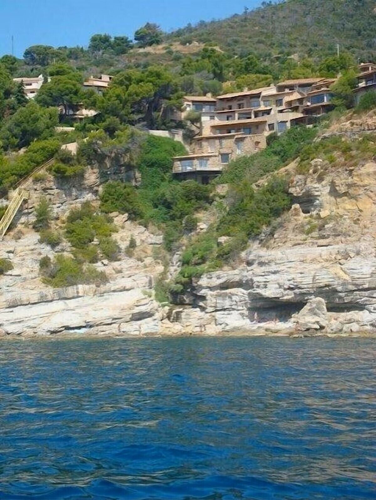 A coastal building with multiple balconies, situated on a rocky hillside with a view of the sea.