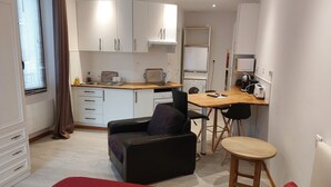 Un espacio habitable compacto con kitchenette, comedor y zona de estar con sofá y mesita.