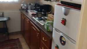 A kitchen with wooden cabinets, a refrigerator with magnets, a microwave, and a gas stove. - Entire home cozy and ideally located (Saint-Denis)