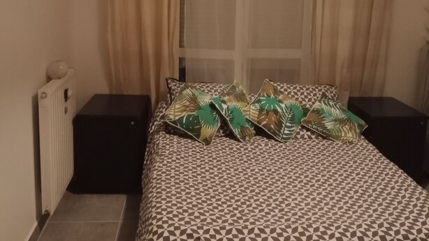 A bedroom with a patterned bedspread, a radiator, a bedside table, and a hanging light fixture. - Entire home cozy and ideally located (Saint-Denis)