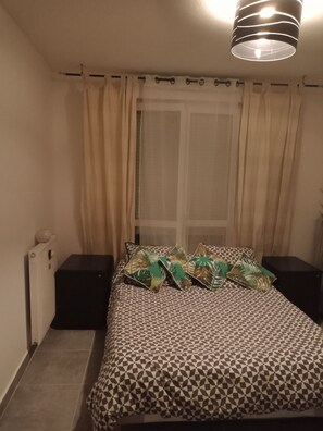 Un dormitorio con una colcha estampada, un radiador, una mesita de noche y una lámpara colgante.