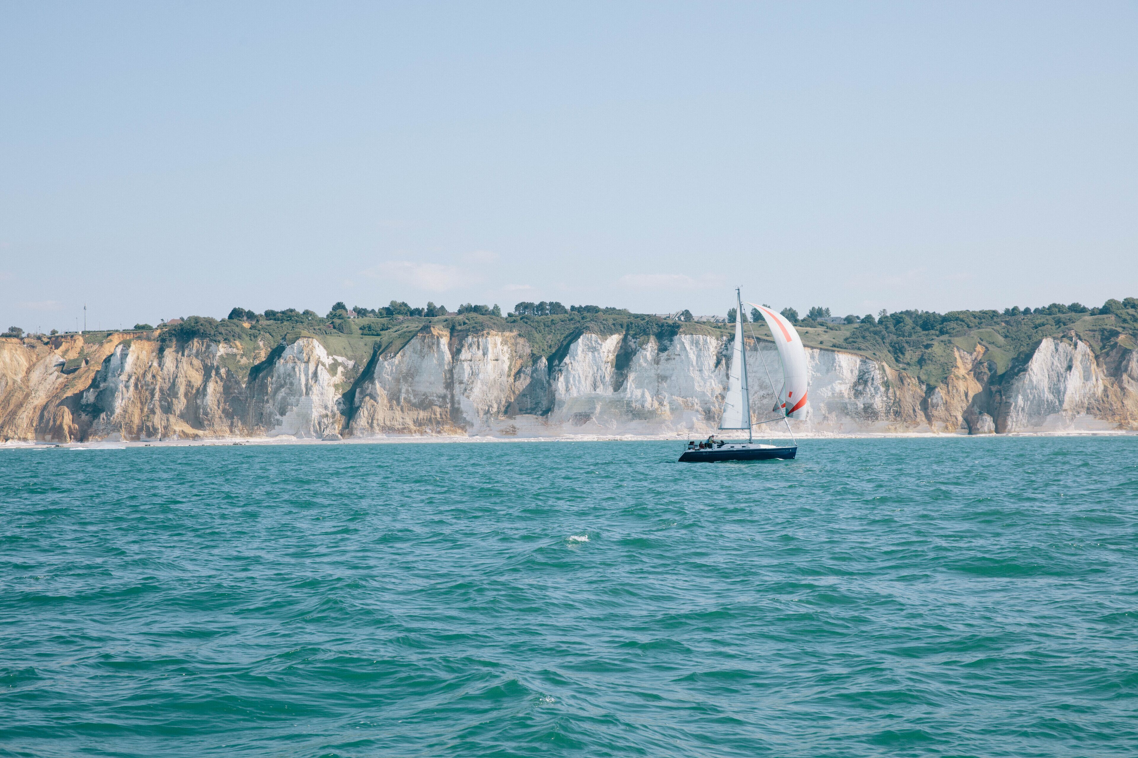 A sailboat on a calm sea with a rocky coastline in the background.