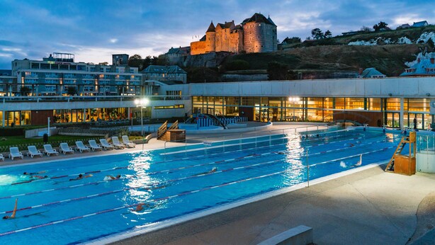 Piscina com várias pistas, um castelo ao fundo e um edifício de hotel com design moderno.
