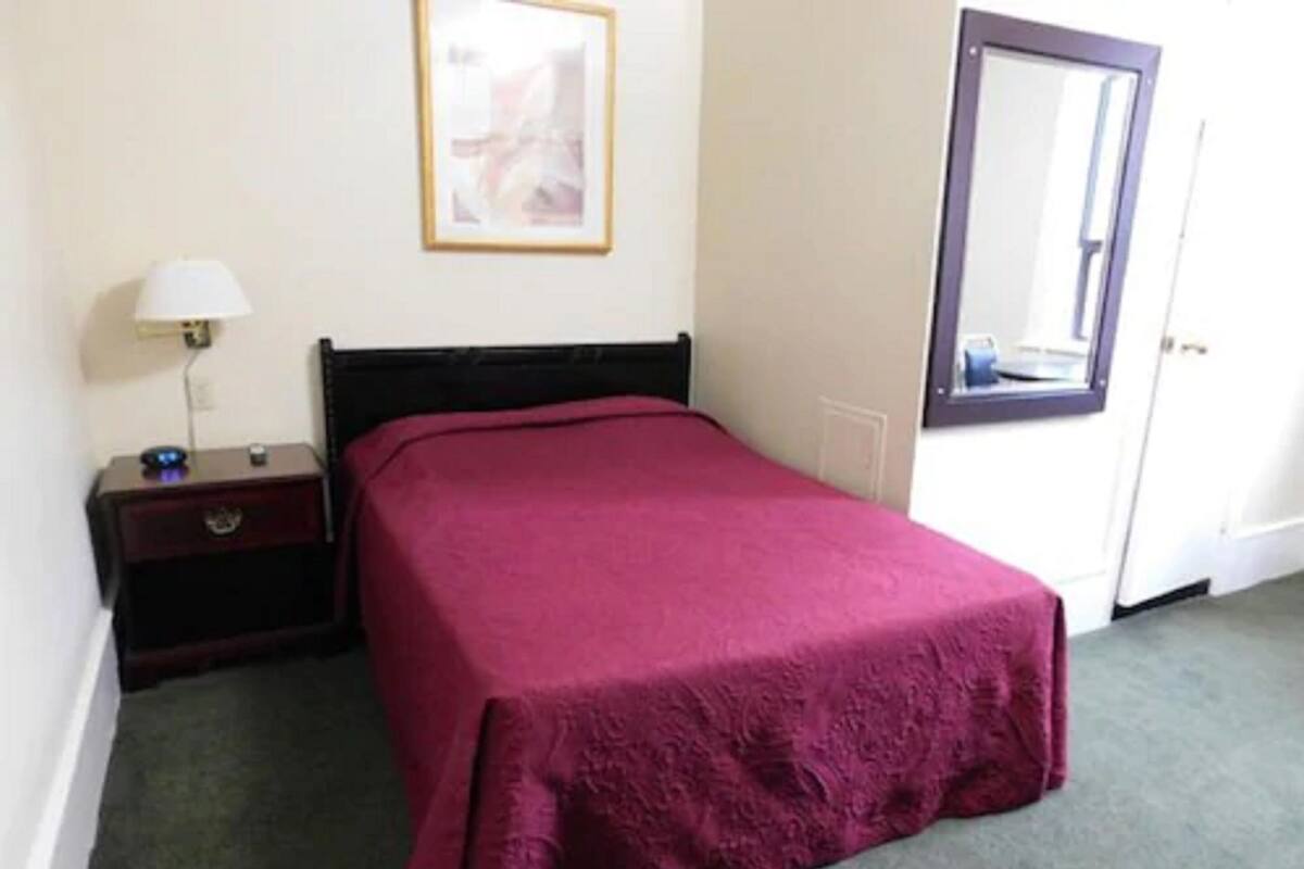 A bedroom with a bed, a nightstand, a lamp, a framed picture on the wall, and a door with a mirror.