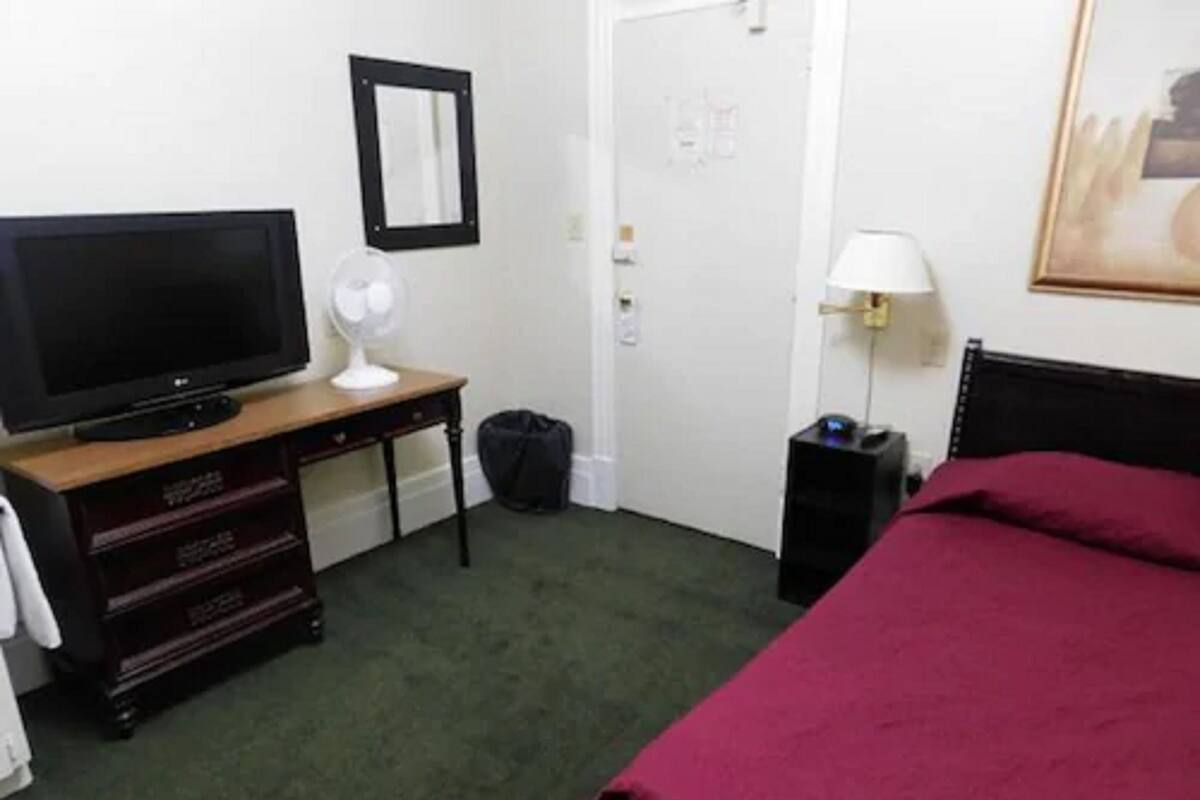 A hotel room with a bed, a television on a wooden dresser, a mirror, a door, and a lamp.