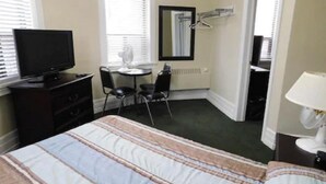 A hotel room with a bed, a TV, a desk with a chair, a mirror, and a radiator. - Filmores Hotel (Toronto)