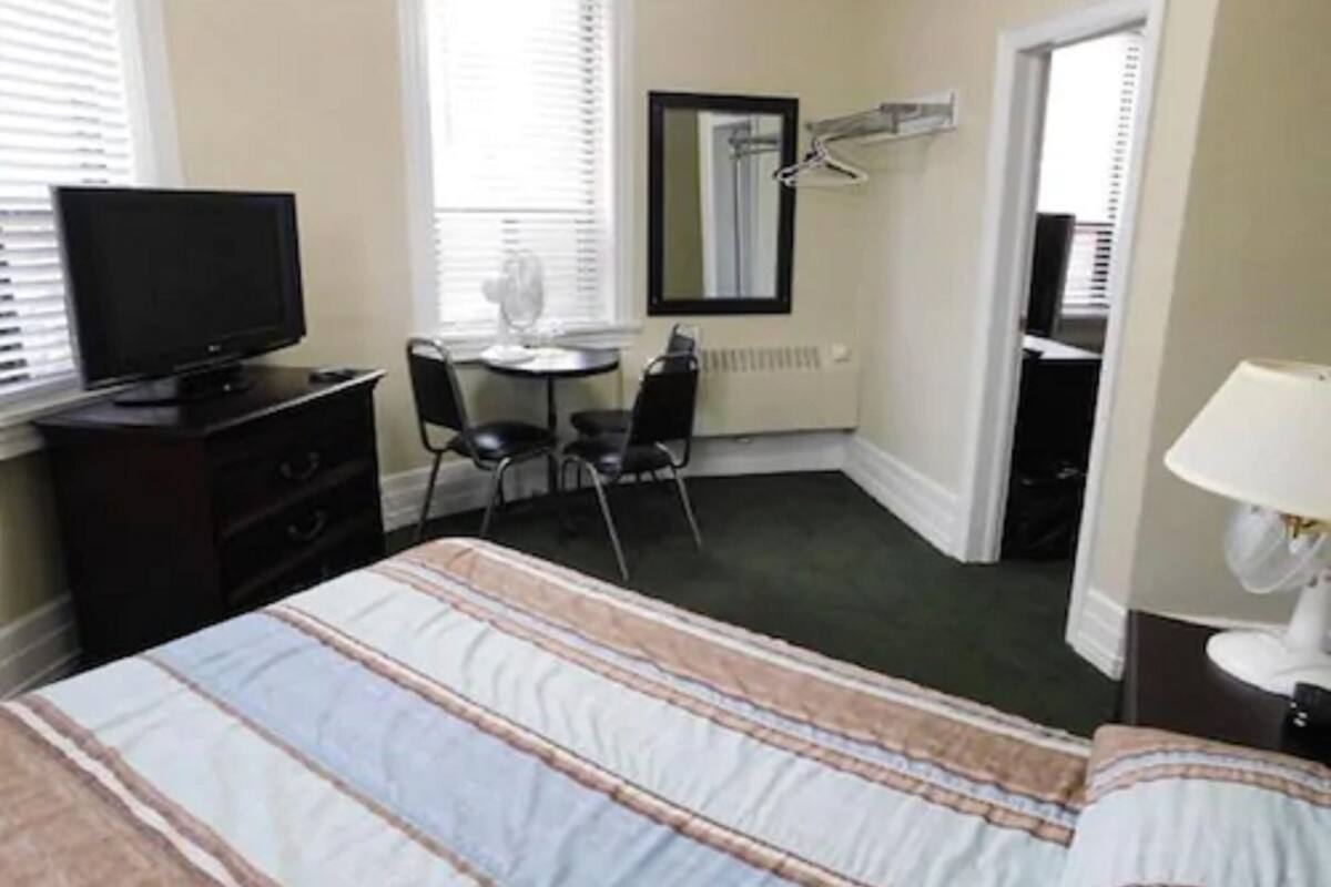 A hotel room with a bed, a TV, a desk with a chair, a mirror, and a radiator.
