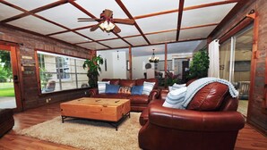 Een ruime woonkamer met een houten plafond, leren banken, een houten salontafel en grote ramen met uitzicht op het omliggende landschap.