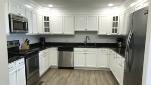 A modern kitchen with white cabinetry, stainless steel appliances, and a wooden floor. - Boardwalk Beauty! Two-Story Oceanview Condo (Rehoboth Beach)