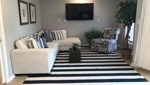 A living room with a sectional sofa, a patterned armchair, a flat-screen TV, and a large striped rug. - Boardwalk Beauty! Two-Story Oceanview Condo (Rehoboth Beach)