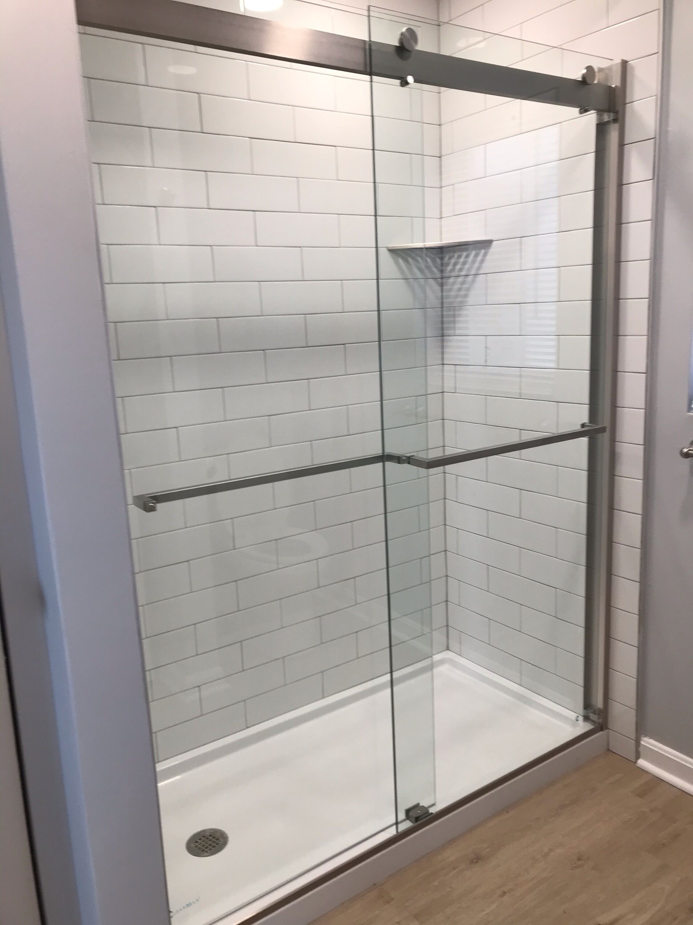 A glass-enclosed shower with white tiled walls and a metal frame.