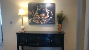A dark blue console table with three drawers, a decorative lamp, and a wall-mounted painting of an octopus. - Boardwalk Beauty! Two-Story Oceanview Condo (Rehoboth Beach)