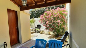 A covered patio with a table and chairs, a wooden door, and a view of a garden with pink flowers.