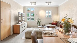 A living room with a sofa, a dining table set for four, a TV, and a large window with a view of buildings. - Saint Tropez, exclusive apartment, heart of the village, Place de la Garonne. (Saint-Tropez)