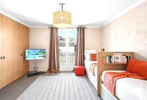 Ein Hotelzimmer mit Fernseher, Bett, Bücherregal, einem Fenster mit Vorhängen und Blick auf Gebäude.