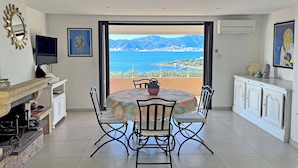 A dining area with a table and chairs, a television, a fireplace, and a view of the sea and mountains. - T4 - 95 m2, Porticcio, garden, garage option, large bedding 180+160. Wifi Fiber (Grosseto-Prugna)