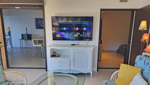 A living room with a glass-top table, wicker chairs, a white cabinet, and a television mounted on the wall. - T4 - 95 m2, Porticcio, garden, garage option, large bedding 180+160. Wifi Fiber (Grosseto-Prugna)