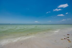 A beach with clear water, a sandy shore, and a distant boat. - Vacation Villas #631 Peaceful Beachside Condo (Fort Myers Beach)