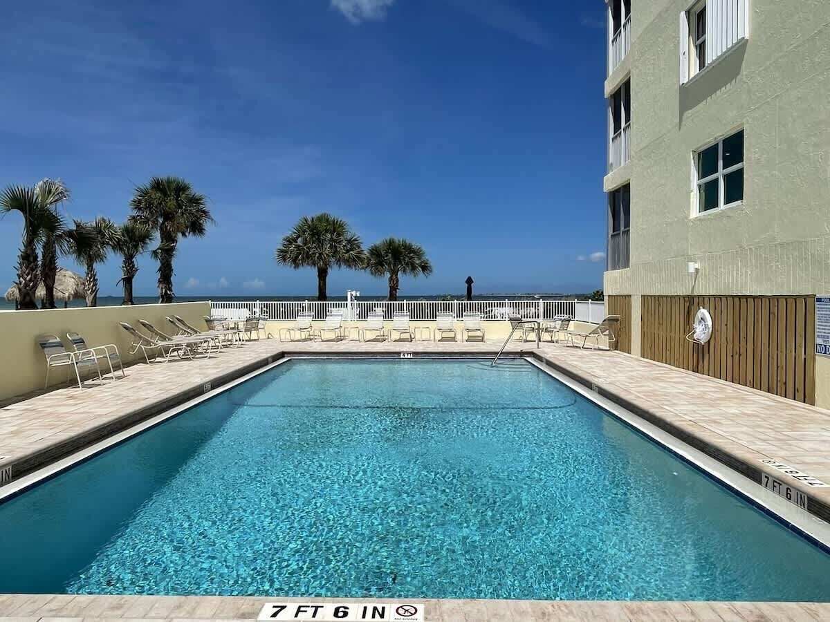 Une piscine rectangulaire à l’eau d’un bleu cristallin, entourée de chaises longues et de palmiers.