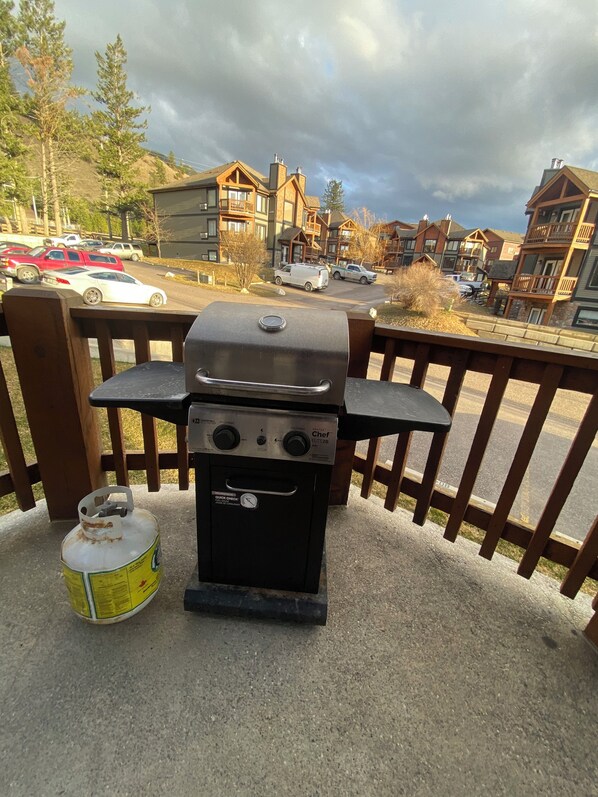 A portable gas grill on a balcony with a view of a residential area and parked cars. - Affordable Cozy Mountain Condo: 2 Balconies, King Bed & BBQ – Radium Hot Springs (Radium Hot Springs)