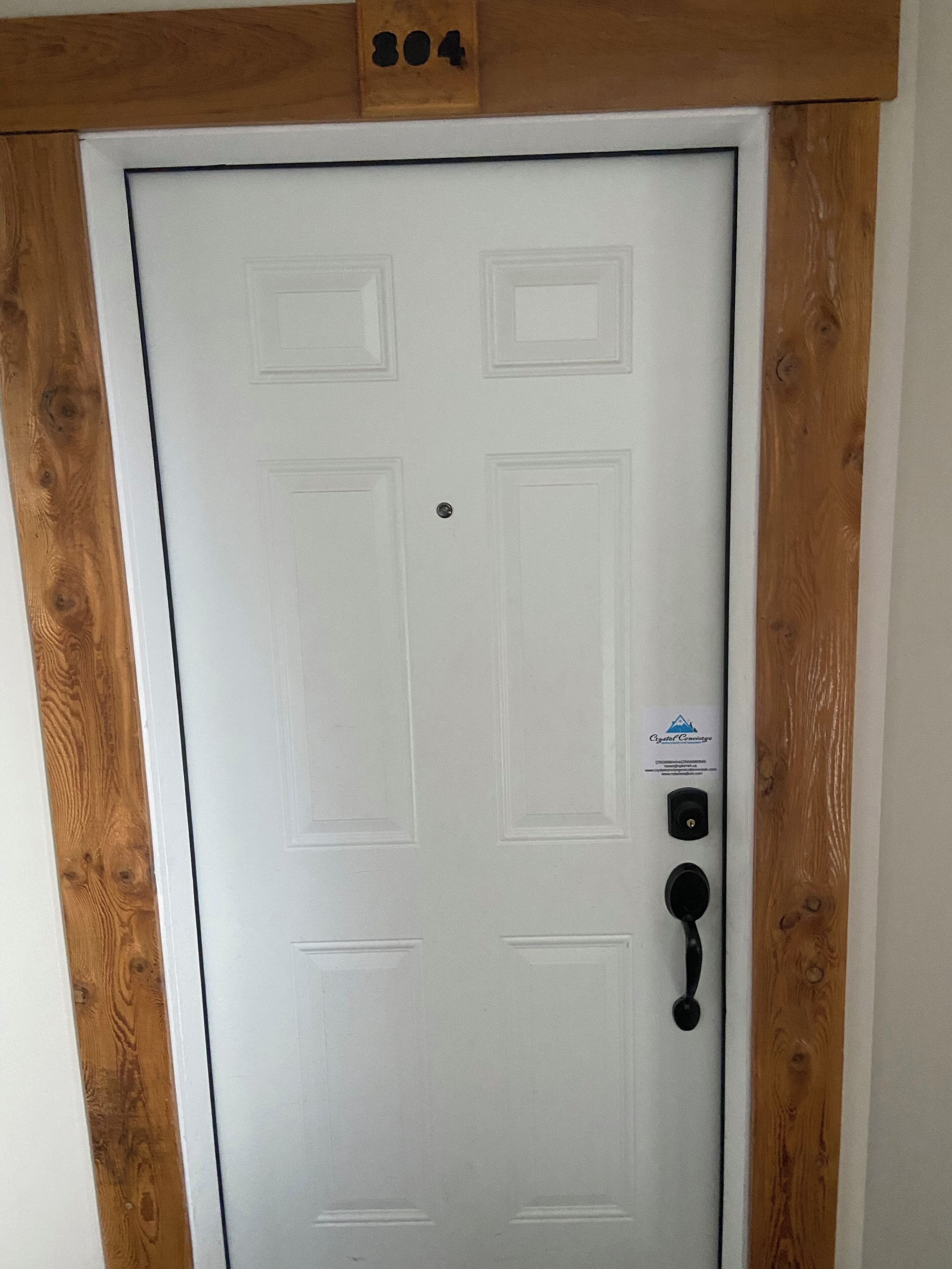 A white door with a wooden frame, a doorbell, and a small sign above the door.