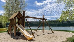 A wooden play structure with a slide and swings on a sandy ground. - Cozy Cabin on the River. 1 Bed 1 Bath Patio w/  BBQ (Breckenridge)