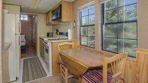 A compact kitchen with a dining area, a refrigerator, a microwave, and a window providing a view of the outdoors. - Cozy Cabin on the River. 1 Bed 1 Bath Patio w/  BBQ (Breckenridge)