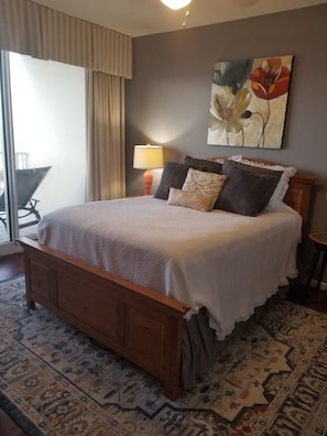 A neatly made bed with a white bedspread and multiple pillows, a bedside lamp, and a floral painting on the wall.