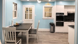 A kitchen with a dining area, white cabinets, a black stove, and a ceiling fan.