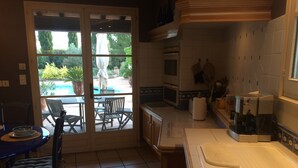 A kitchen with a large window, a dining area with chairs, and a sink. - Charming villa with private pool (Arles)