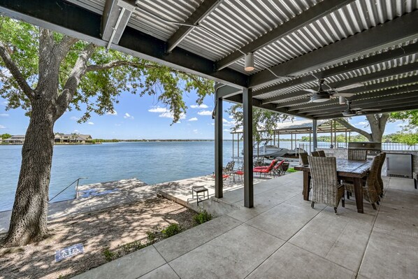 A covered patio with a table and chairs, overlooking a body of water.