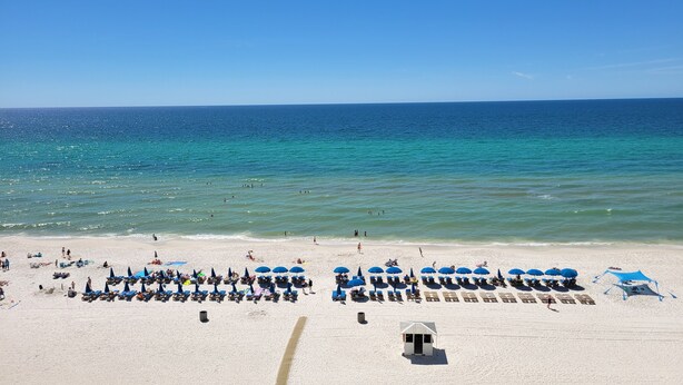 A beach with rows of sun loungers and umbrellas, a lifeguard tower, and a clear view of the ocean.