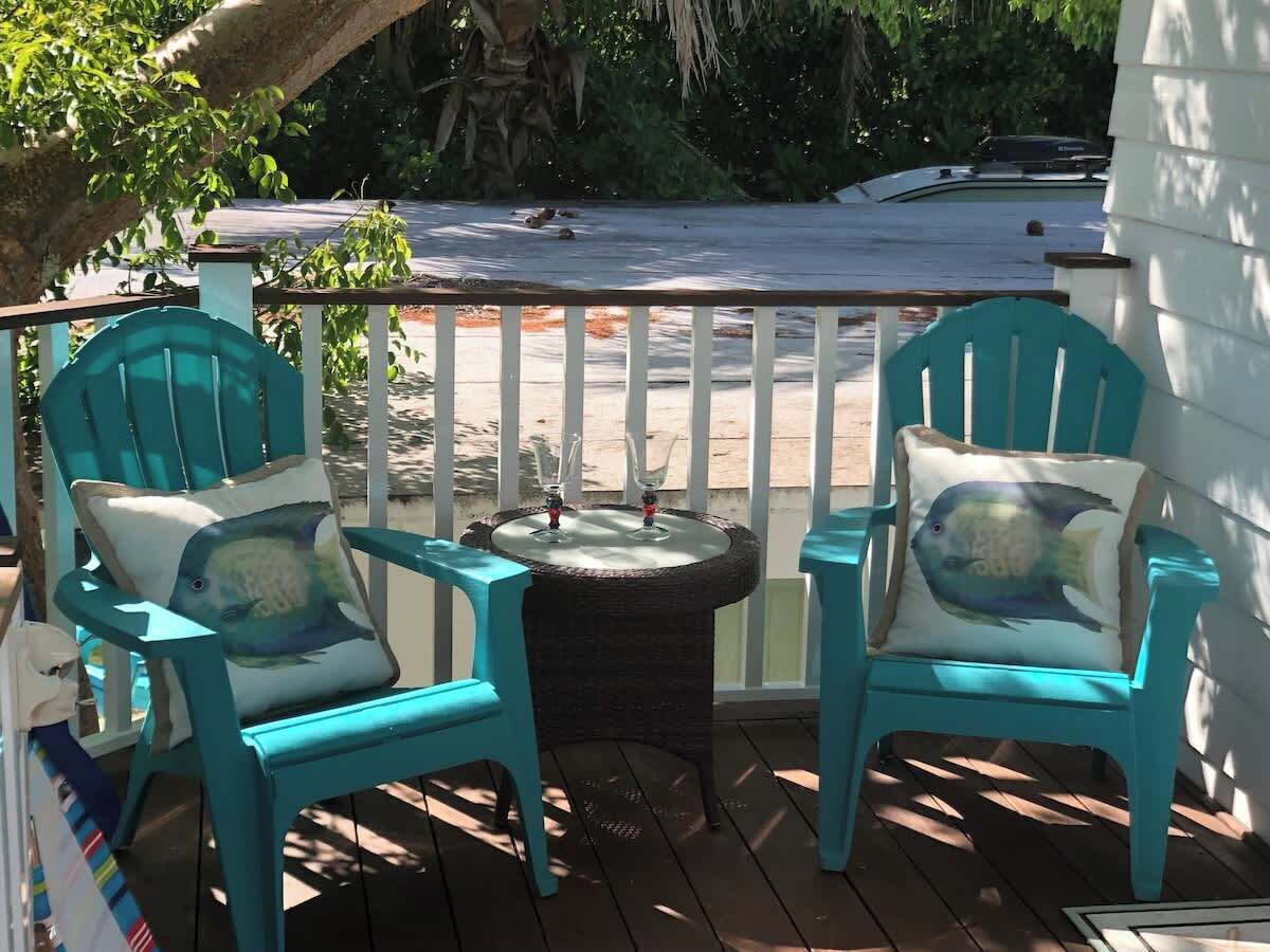A covered outdoor seating area with two turquoise chairs and a small round table, surrounded by a white fence.