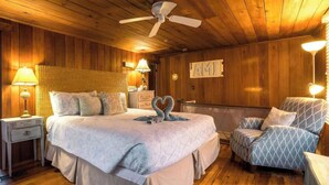 A cozy bedroom with a large bed, a chair, a nightstand, a lamp, and a ceiling fan. - Gulf Front Guest House (Anna Maria)