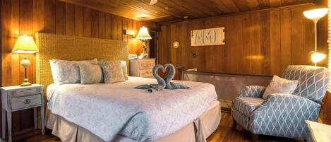A cozy bedroom with a large bed, a chair, a nightstand, a lamp, and a ceiling fan.