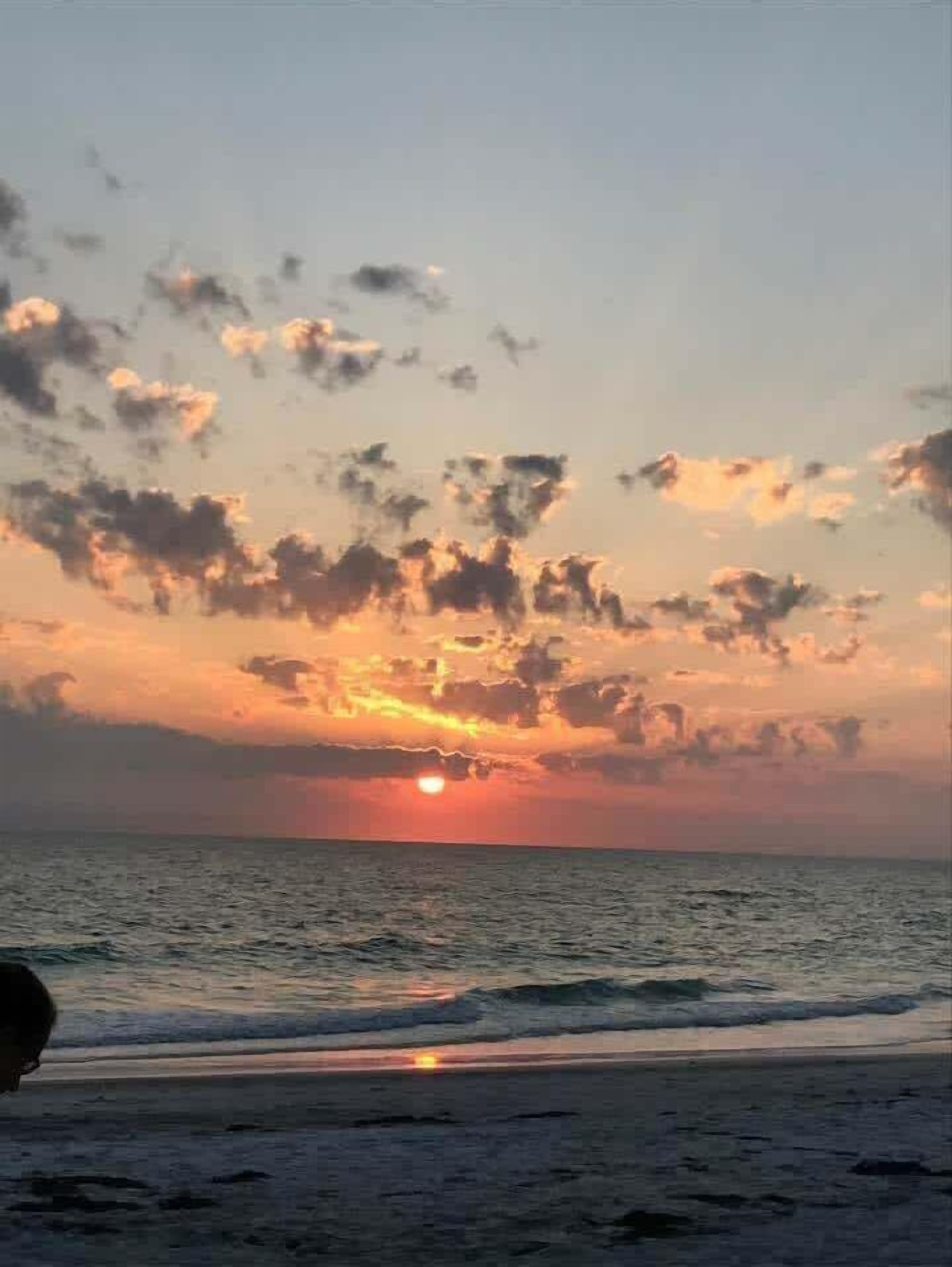 A sunset over the ocean with clouds in the sky.
