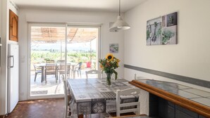 A kitchen with a dining area, a refrigerator, a table with a vase of flowers, and a view of the outdoors. - Pleasant, sunny villa (Vaison la Romaine)