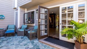 Un patio con mobiliario de mimbre y suelo de piedra, una puerta que da al interior y una planta en maceta.