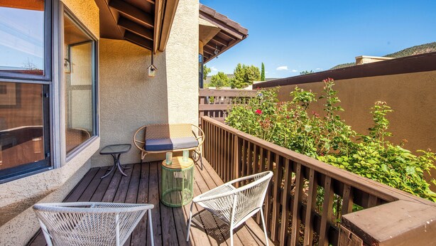 Un balcone con pavimento in legno, un tavolo con sedie e vista sul verde.