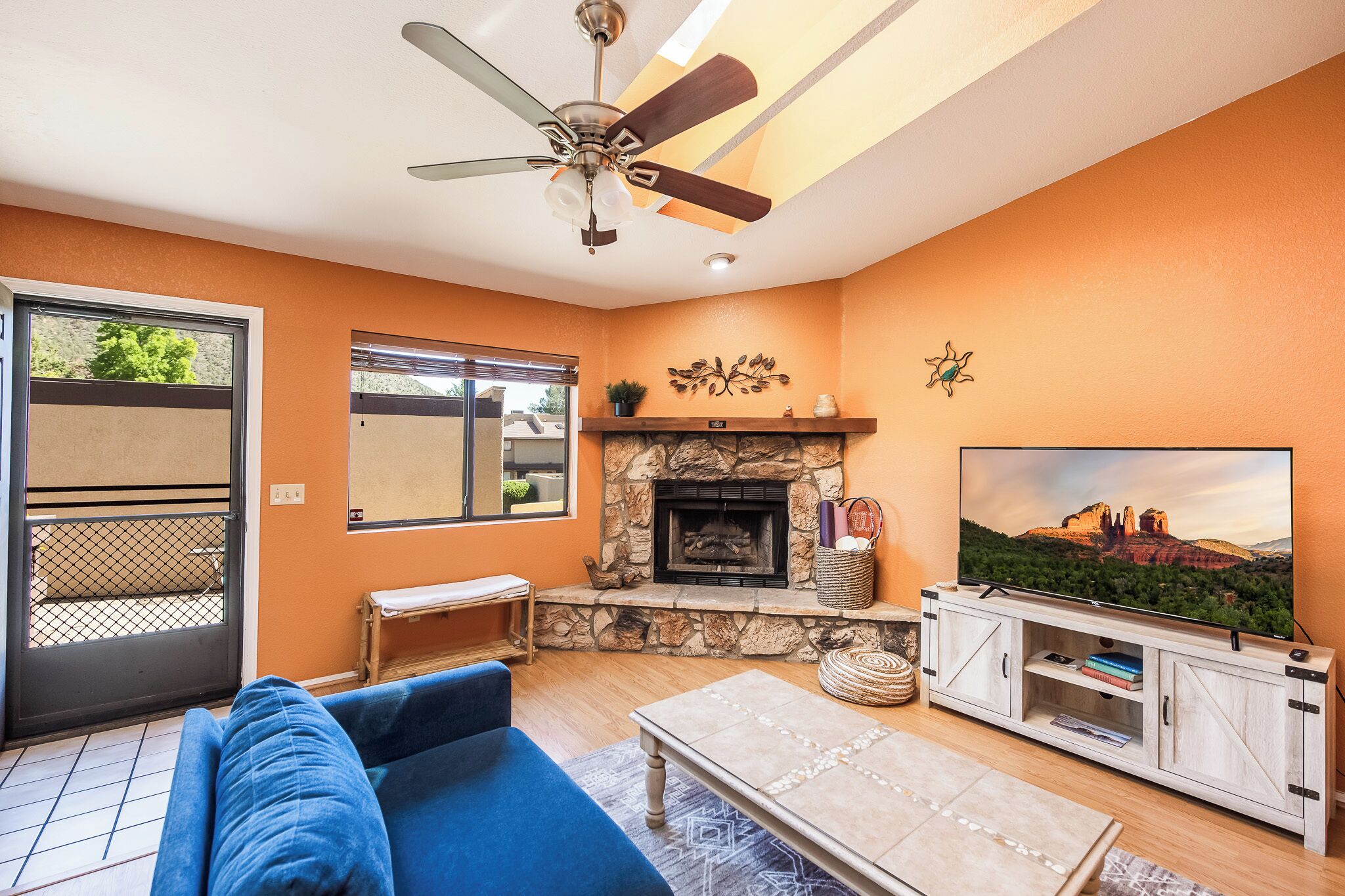 Una sala de estar con chimenea, ventilador de techo, televisor y sofá.