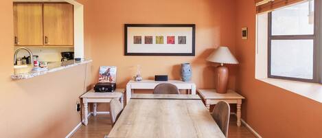 A dining area with a wooden table, chairs, a chandelier, a framed picture, and a window.