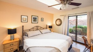 Una camera da letto con un letto, lampade da comodino, una ventola a soffitto, una finestra con tende e uno specchio fissato al muro.