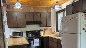 Una cocina con armarios de madera, estufa, microondas, refrigerador y luces colgantes.