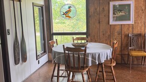 Comedor con una mesa redonda, sillas de madera, ventilador de techo, ventana con un diseño de vidrio emplumado y un cuadro de un pez en la pared.