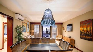 Un comedor con mesa de vidrio, sillas de mimbre, una lámpara colgante y vistas al exterior a través de amplios ventanales.